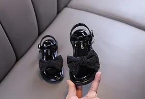 Detailed view of black patent leather girl's sandals with a decorative lace bow
