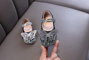 Detailed view of the sparkling rhinestone butterfly on girls' black leather princess shoes.