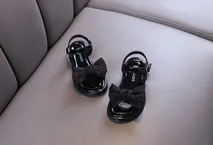 Detailed view of black patent leather girls' sandals with lace bow and buckle strap