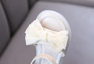 Close-up detail of cream girl's sandal featuring a delicate lace bow decoration.