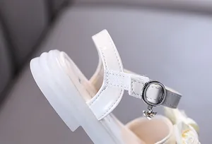 Close-up detail of white patent leather girls princess sandal featuring buckle strap and charm
