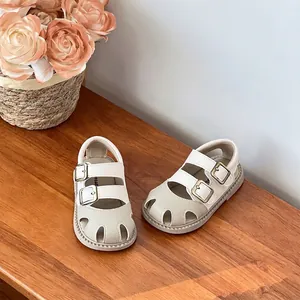 Primer plano de sandalias para bebé color crema con hebillas sobre mesa de madera.