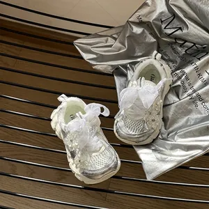 Zapatillas plateadas de niña con flores y cordones de cinta en superficie metálica
