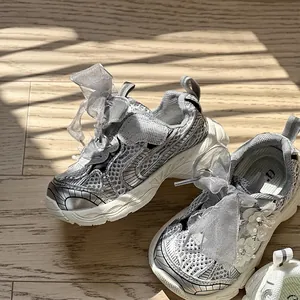 Vista detallada de zapatillas plateadas para niña con lazos y hermosos detalles florales