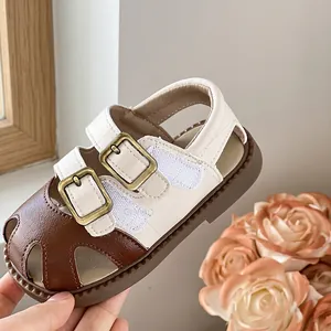 Primer plano de sandalias para bebé blanco y marrón con diseño calado.