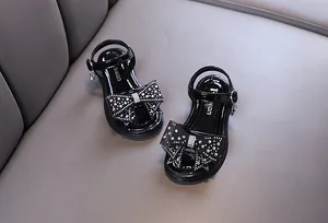 Detalle de sandalias negras para niña con lazo de strass y suela de moda.