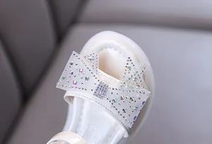 Vista detallada del lazo de diamantes de imitación brillantes en las sandalias de princesa blancas.