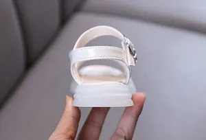 Detalle macro que muestra el charol blanco brillante y la suela gruesa de las sandalias de niña