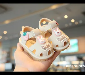 Primer plano de adorables sandalias para bebé crema con parches de conejo y fresa