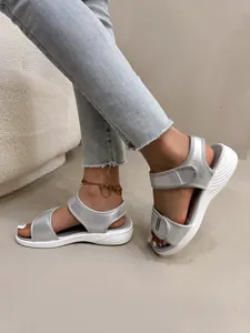 Détail latéral de sandales de sport argentées pour femmes avec velcro et semelles blanches.