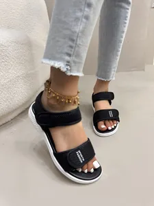 Gros plan sur des sandales de sport noires pour femmes avec velcro et semelle compensée blanche.