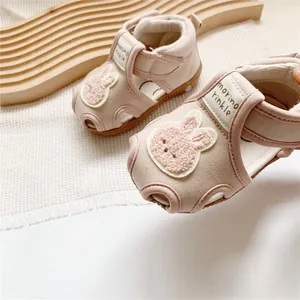 Close-up of pink baby sandals featuring a plush cartoon rabbit and velcro strap detail.