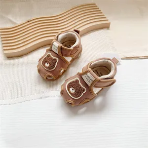 Close-up of brown cartoon bear baby sandals with Velcro straps on a wooden prop.