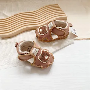 Close-up of brown baby walker sandals with cute cartoon bear patch and velcro strap.
