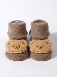 Detail showing the thick knitted texture and plush bear patch on brown baby floor socks