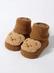 Detailed view of thick brown baby socks with a soft plush bear face patch decoration.
