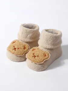 Close-up detail of thick beige baby terry socks featuring a cute plush bear patch