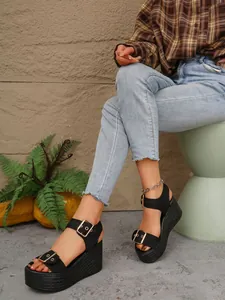 Close-up of black platform wedge sandals with adjustable gold buckles on a model