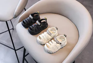 Sandales fermées pour bébés en noir et blanc présentées sur une chaise beige