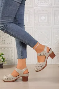 Detailed macro view of beige hollow-out closed-toe sandals with a wooden block heel.