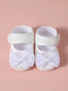Détail de chaussures bébé en dentelle blanche avec nœuds et semelle souple.