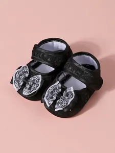 Détail de chaussures de princesse noires pour bébé avec nœud en dentelle blanche et semelle souple.