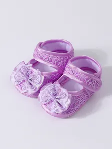 Gros plan de chaussures de bébé fille en dentelle violette avec semelles souples et fleurs.