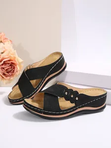 Détail de sandales compensées noires avec brides croisées ajourées et clous