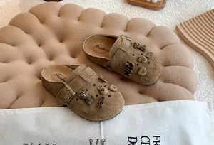 Detailweergave van bruine suède kinderklompen met schattige beer- en bloembedeltjes.