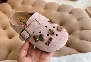Detail van roze suède kinderklompen met schattige berenhangers en riempje.
