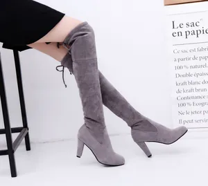 Detail of gray suede over-the-knee high heel boots with tie-back laces on a model.