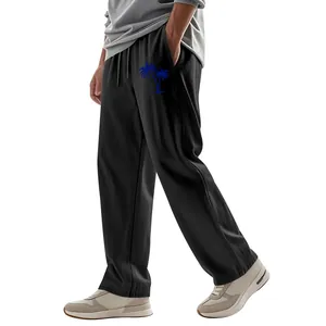 Detail view of men's loose linen trousers with blue palm tree print on black fabric
