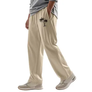 Detail view of men's loose linen trousers with tropical palm tree print in beige color.