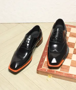 Close-up detail of black patent leather Oxford shoes with distinctive orange welt trim.