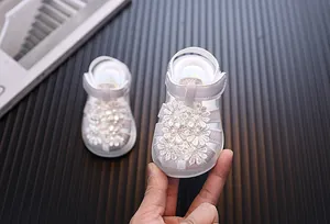 Nahaufnahme von Babymädchen Sandalen mit weißen Spitzenblumen und Perlen