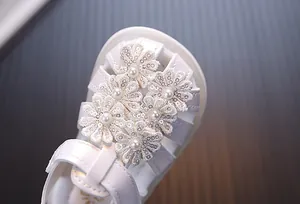 Nahaufnahme weißer Lauflern-Sandalen mit bestickten Blumen-Pailletten und Perlen.