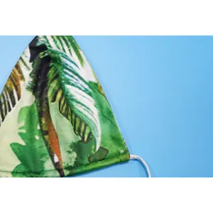 Close-up detail of tropical palm leaf print bikini top fabric against blue background.