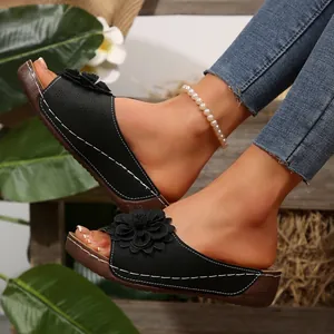 Detalle de sandalias con cuña negras con un elegante adorno floral y diseño calado único.