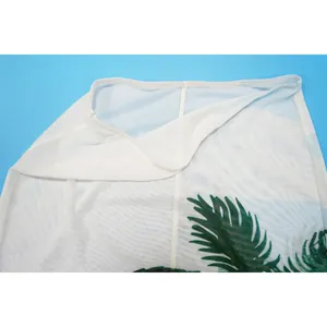 Close-up of white mesh beach cover-up skirt with tropical green palm leaf print detail.