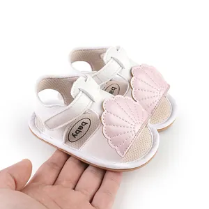 Detailed view of white baby sandals with pink shell accents held by hand