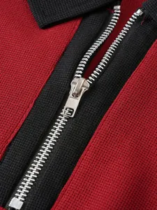 Detaillierte Nahaufnahme eines silbernen Halbreißverschlusses an einem rot-schwarzen Polohemd.
