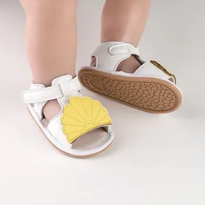 Close-up of white baby sandals featuring yellow shell decoration and non-slip rubber sole