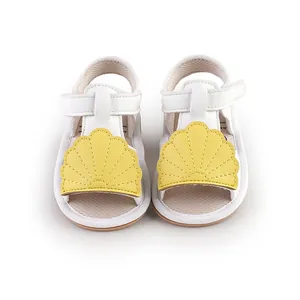 Detail view of white baby walking sandals with yellow shell decoration and velcro strap.