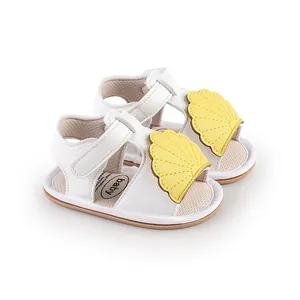 Close-up of white baby sandals featuring yellow shell decorations and velcro straps