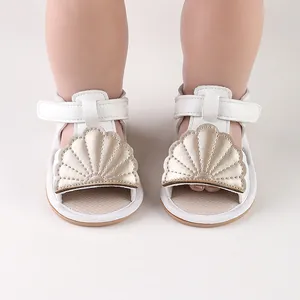 Close-up detail of white baby summer sandals with a unique gold shell decorative pattern
