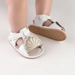 Close-up of white infant summer sandals with a golden shell decor and velcro strap