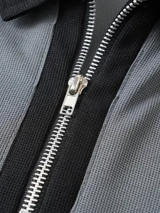 Nahaufnahme des Metallreißverschlusses an einem grau-schwarzen strukturierten Herren-Polo.