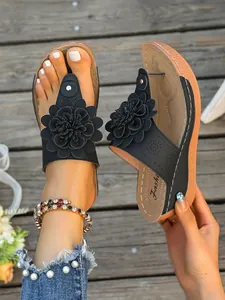 Detailansicht der schwarzen Keilsandaletten mit großer 3D-Blume und Perlen-Denim-Akzenten.