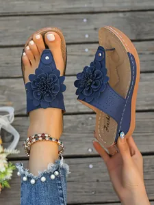 Nahaufnahme blauer Keil-Flip-Flops mit Blumen und eleganter Plateausohle im Retro-Stil