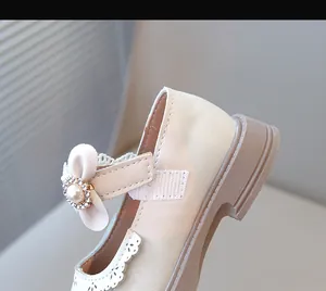Gros plan sur une chaussure de princesse beige pour fille avec nœud perlé et dentelle